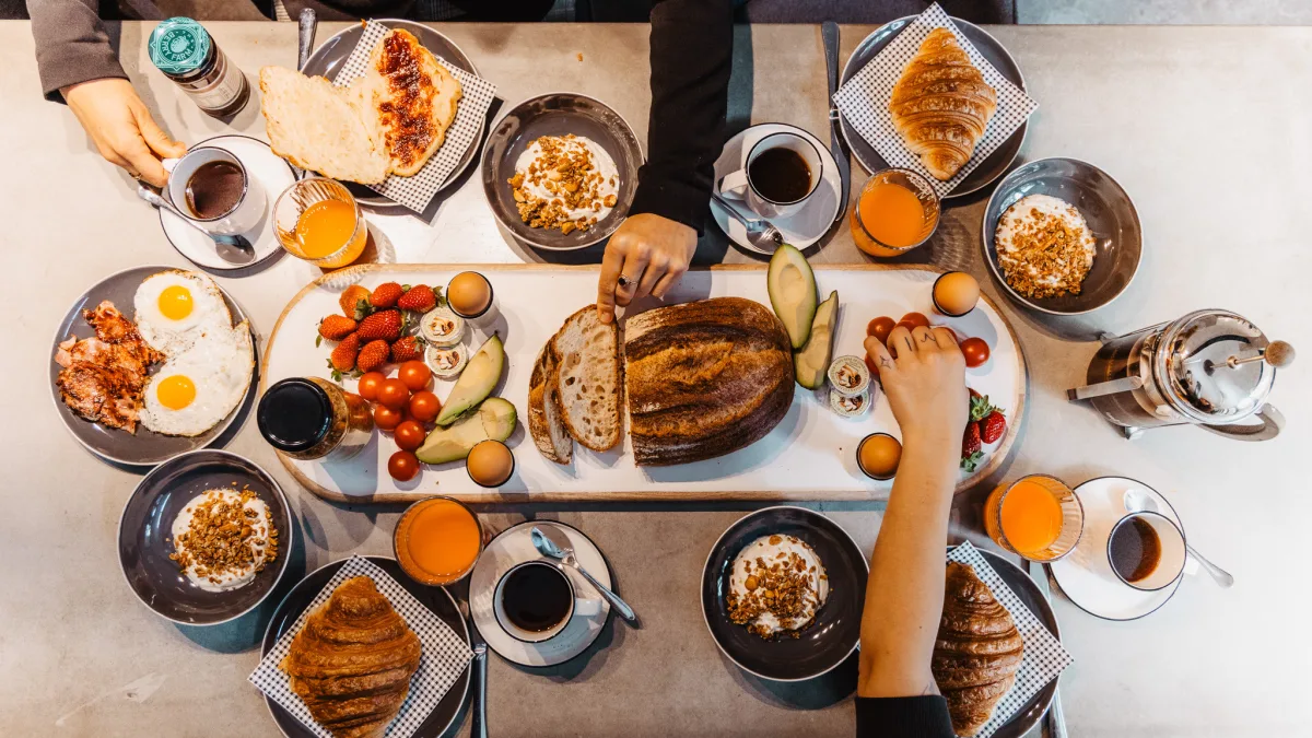 Breakfast hamper ingredients laid out on a table with hands reaching for the food.