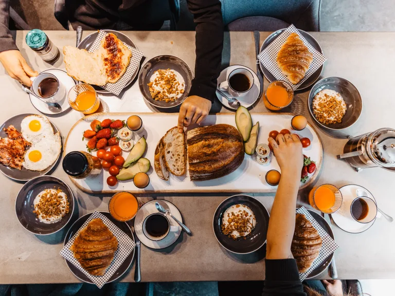 Breakfast hamper ingredients laid out on a table with hands reaching for the food.
